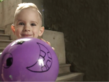 Child smiling and holding a purple ball with smiley face